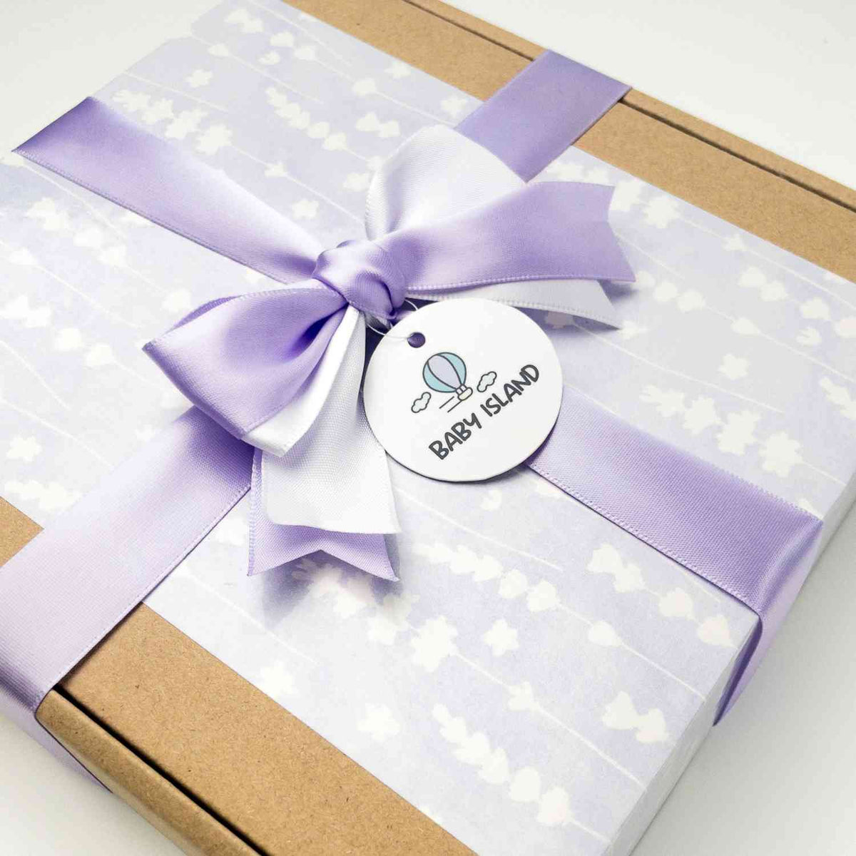 Scatola regalo con fiocco di raso lilla, decorata con stelle bianche, contenente set per neonato con morbida mussola e accessori.