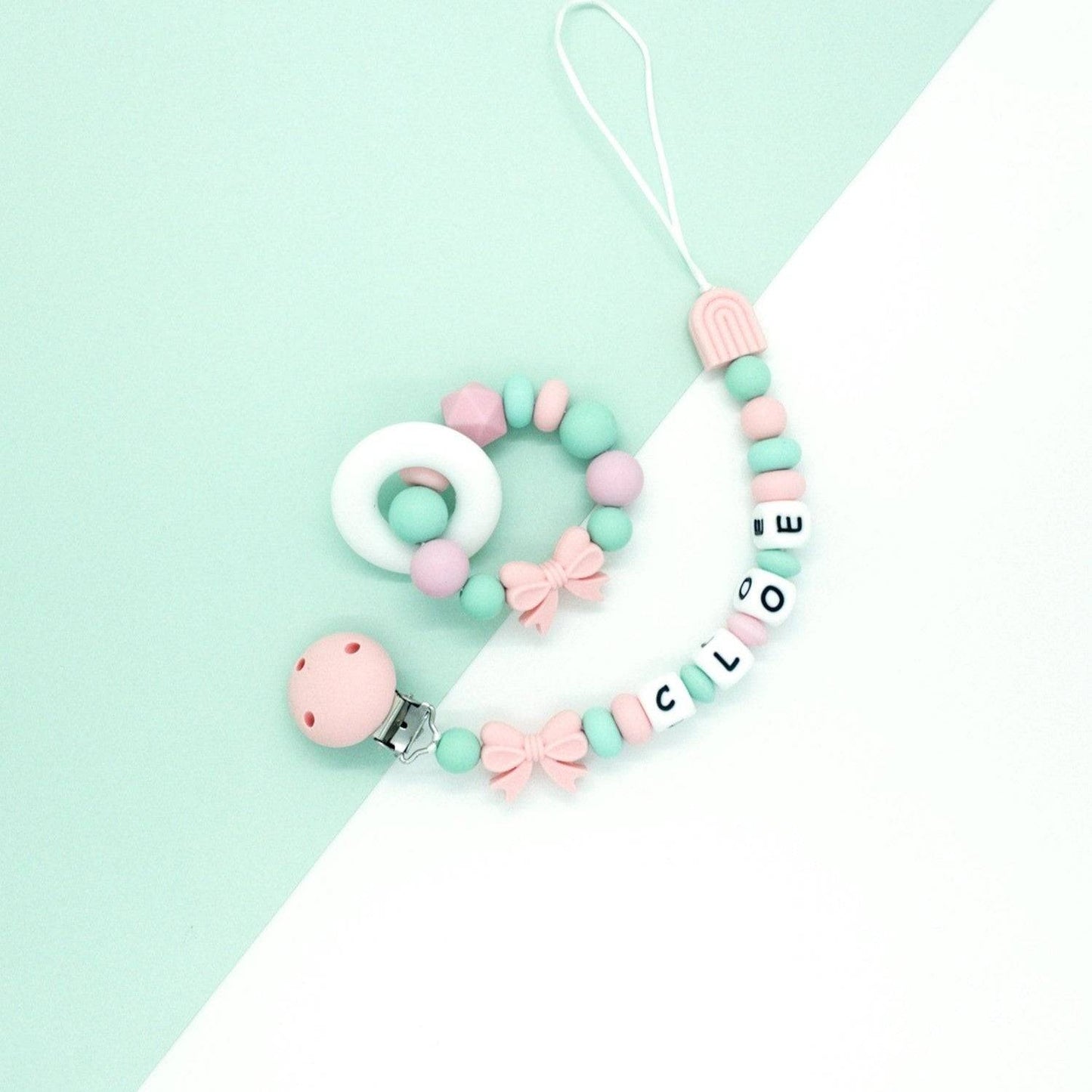Set massaggiagengive ad anello e catenina porta ciuccio personalizzata per neonati con nome in silicone rosa e verde menta, ideale per la dentizione e la sicurezza del ciuccio, design moderno con fiocchetti decorativi su sfondo verde e bianco