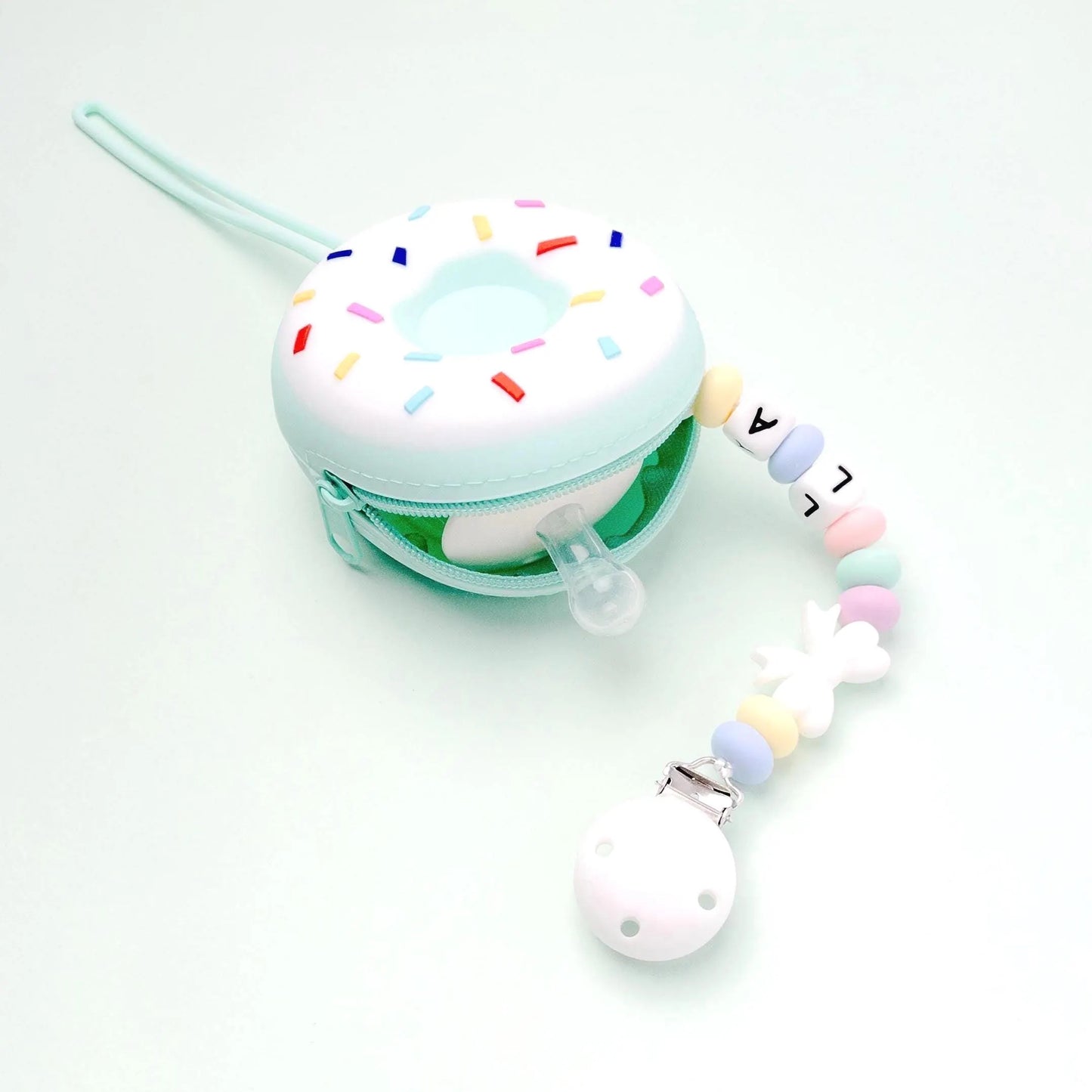Custodia silicone per ciuccio a forma di donut in colori bianco e verde tiffany con cerniera, si può vedere dentro il ciuccio e un pezzo di catenina porta ciuccio che esce.