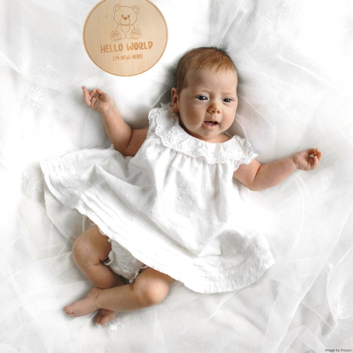 card di benvenuto nascita hello world in legno con orsetto e scritta "hello i'm here" di fianco a bambina neonata sdraiata