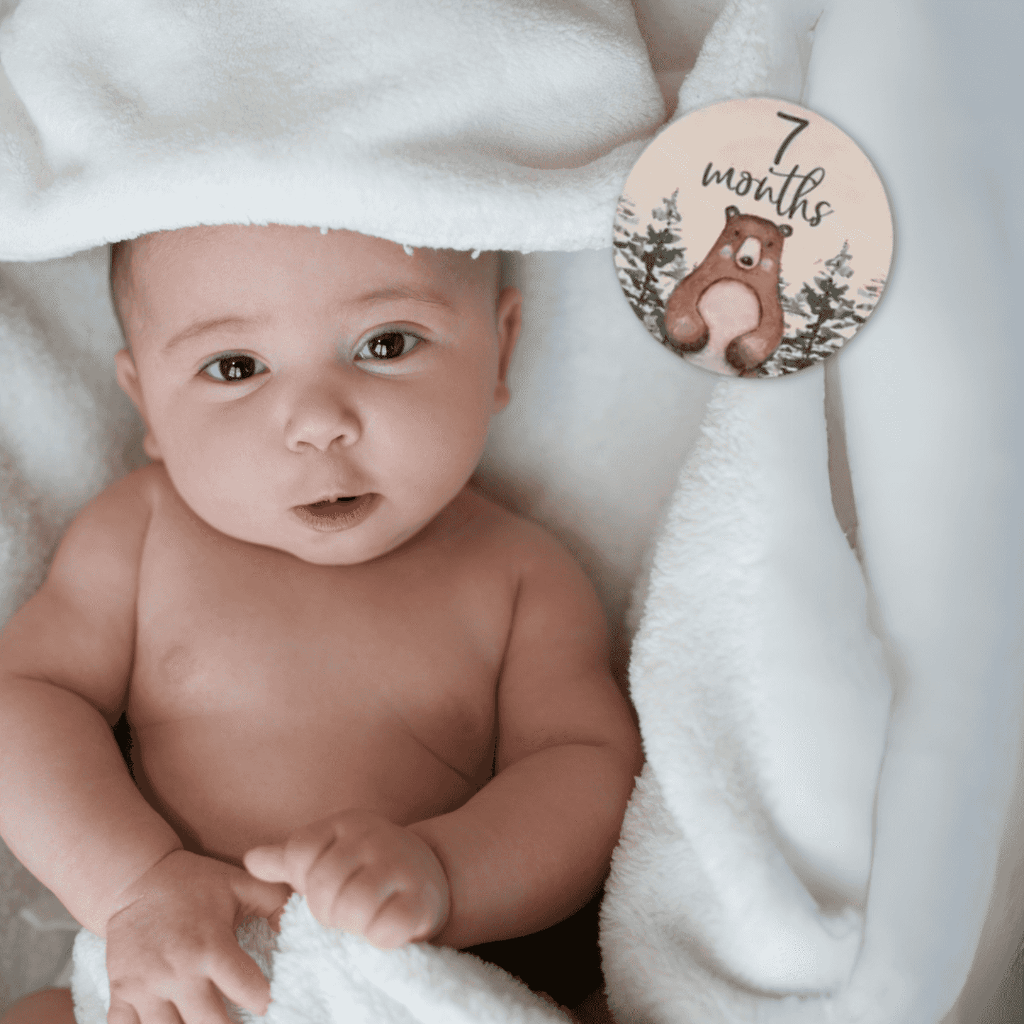 Foto di un neonato sorridente sdraiato su una coperta a tema foresta, affiancato da una milestone card in legno con la scritta “7 months old”. Perfetta per immortalare il settimo mese del bambino, questa immagine è ideale per genitori che desiderano documentare la crescita del proprio piccolo. Parte del set regalo Woodland Adventures, include accessori a tema animali della foresta