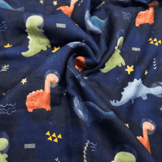 Mussola neonato in cotone e bambù con fantasia di dinosauri colorati su sfondo blu, decorata con stelle e simboli spaziali. Multiuso, morbida, assorbente e certificata OEKO-TEX®