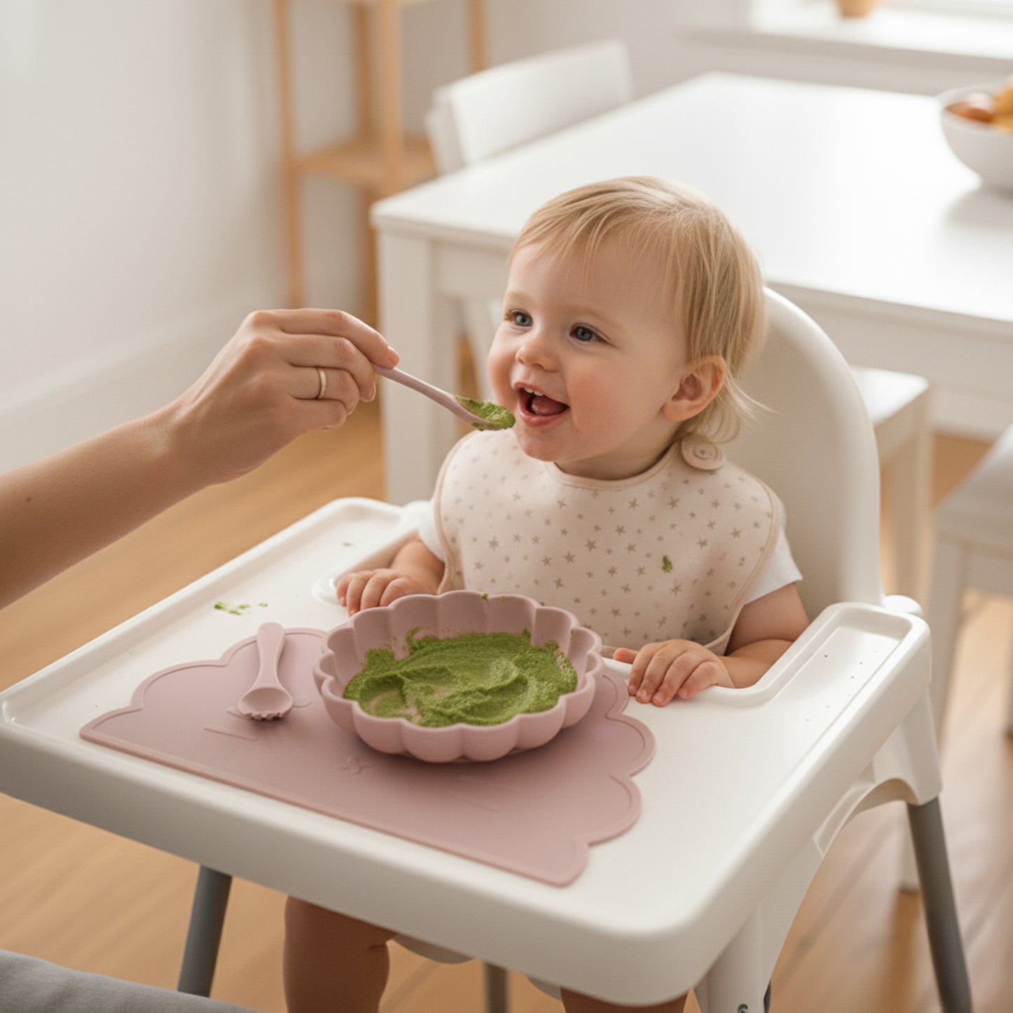 bambina che mangia la sua prima pappa con un set alimentazione in silicone rosa chiaro con piatto, forchette, tovaglietta.
