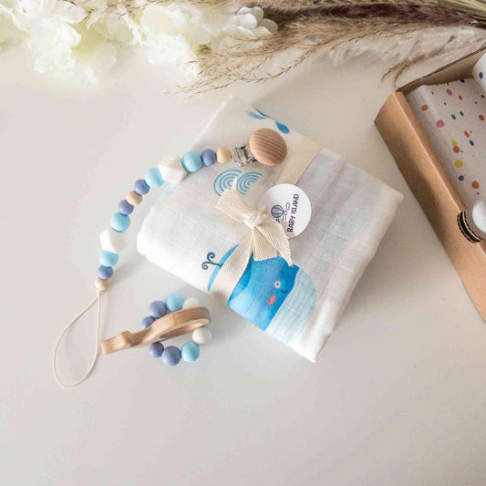 Set neonato a tema balena composto da massaggiagengive in legno e silicone, sonaglio colorato, catenina per ciuccio con perline in silicone, e mussola morbida con stampa balena. Perfetto per stimolare i sensi del bambino e offrire comfort durante la dentizione. Idea regalo elegante e pratica per neonati