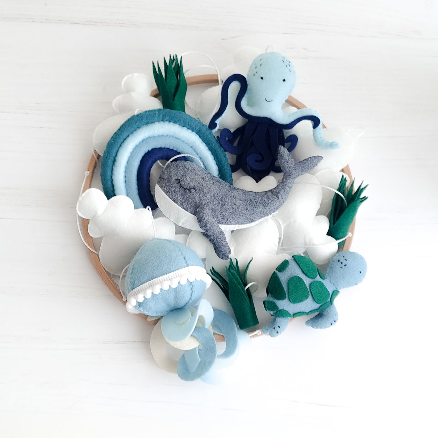 Mobile appeso per lettino con palette colori rilassante blu, verde salvia e grigio. Figure marine in feltro imbottito che fluttuano sotto un cerchio in legno naturale. Include alghe marine e nuvole soffici, ideale per arredamento nursery moderno o stile nordico scandinavo per bambini.