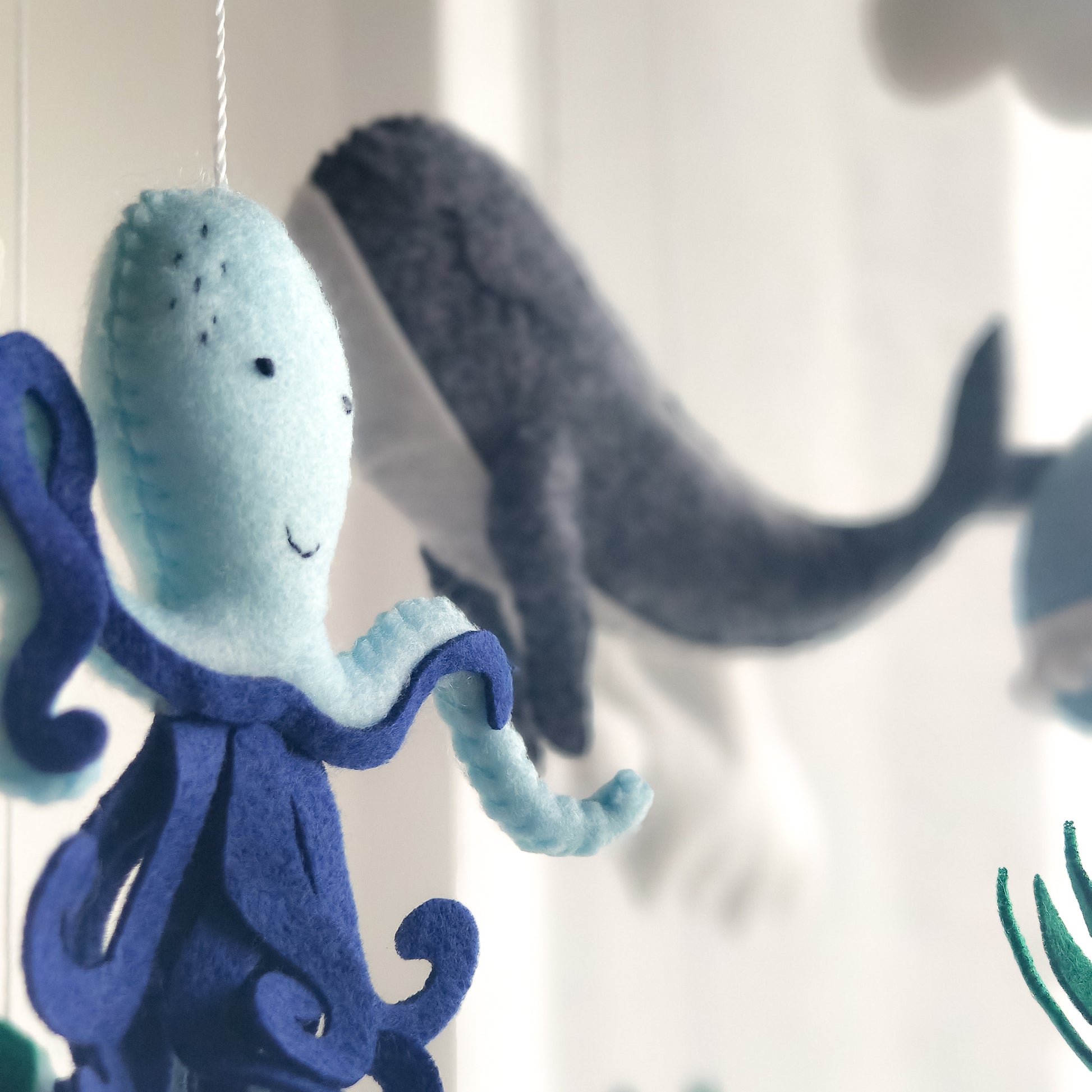 Giostrina artigianale in feltro e legno per la prima infanzia. Cuciture dettagliate su animali marini e arcobaleno imbottito. Design ecologico e sicuro per la vista del neonato, stimola l'attenzione con forme morbide e colori acquatici naturali come il verde smeraldo e il blu navy