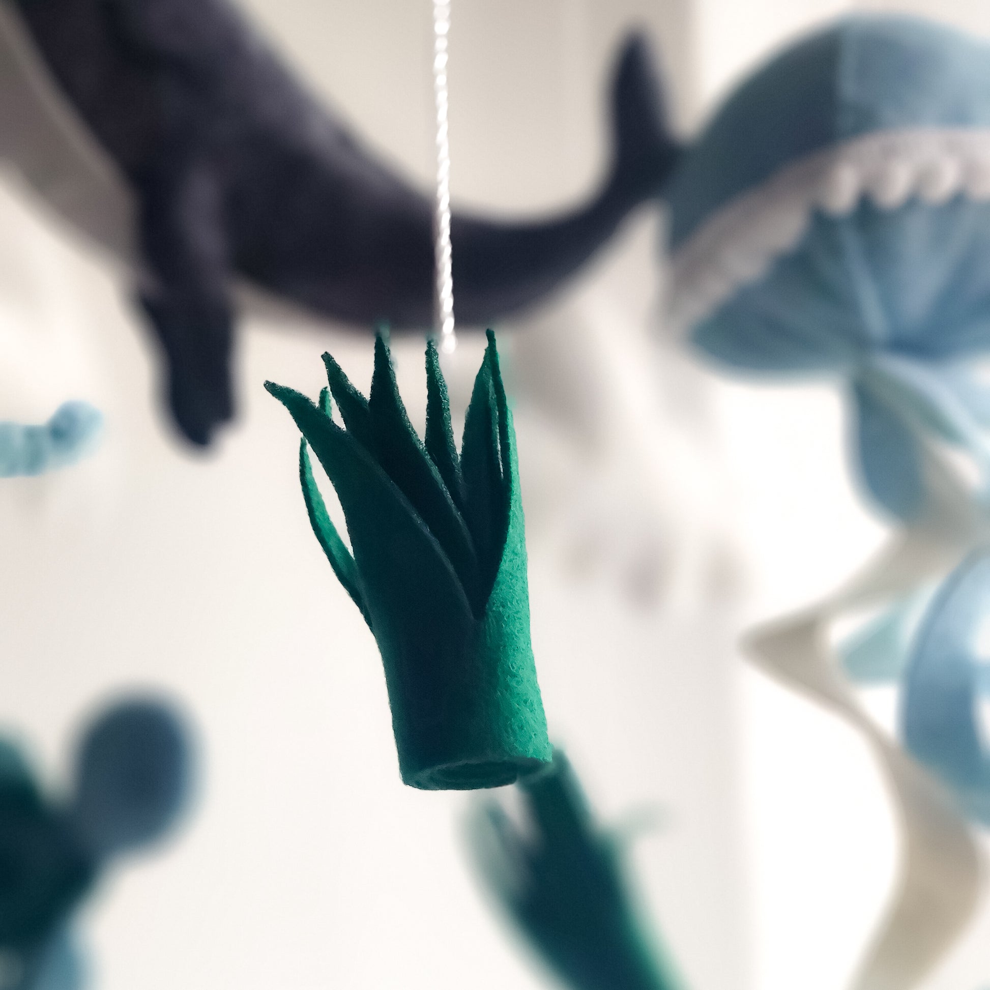 Mobile decorativo in feltro premium con texture morbida. Composizione equilibrata con arcobaleno superiore e pioggia di animali marini e alghe in feltro. I toni freddi e calmanti del blu e del verde lo rendono adatto a culle in legno o bianche in camerette eleganti.