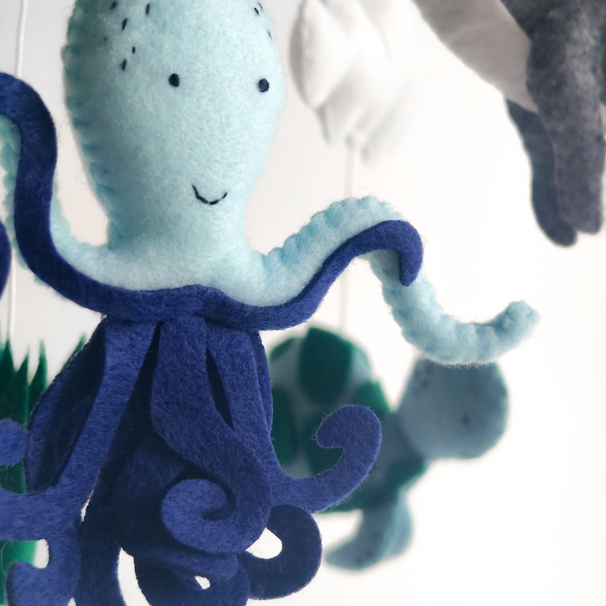 Primo piano di giostrina culla con animali del mare cuciti a mano. Dettagli curati come gli occhi ricamati della balena e le perline decorative sulla medusa. Struttura leggera in legno che permette un movimento dolce e naturale per conciliare il sonno del bebè