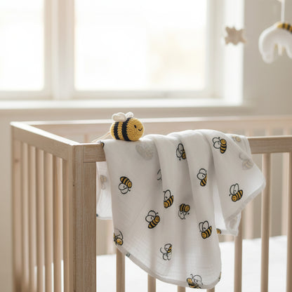 Mussola api neonato in 100% cotone appoggiata su lettino in legno chiaro, ideale per fasciatura e coccole quotidiane. Design unisex con api gialle e nere.
