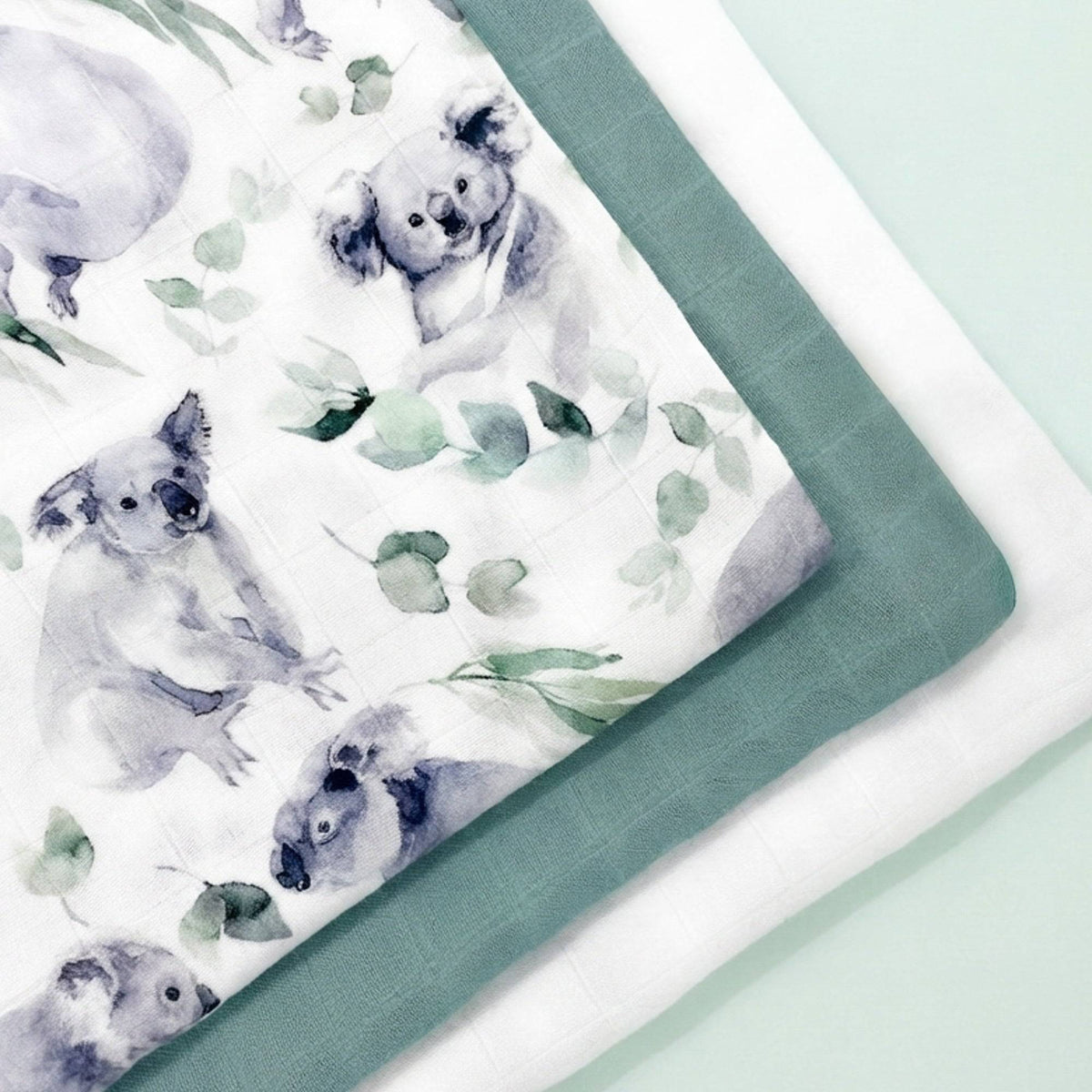 Particolare di mussole in cotone e bambù con disegni di koala e foglie, in tonalità verdi e blu, morbide e leggere.