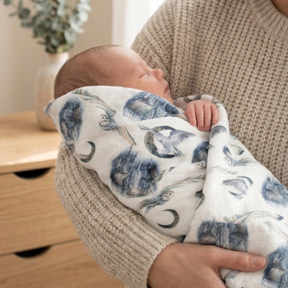 Neonato che dorme su una coperta in mussola di cotone e bambù con fantasia fiabesca blu su bianco, avvolto in morbidezza e comfort
