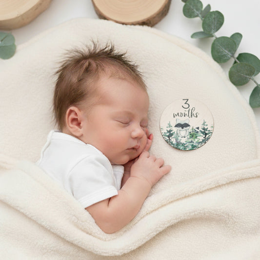 Foto di un neonato sorridente sdraiato su una coperta a tema foresta, affiancato da una milestone card in legno con la scritta “7 months old”. Perfetta per immortalare il settimo mese del bambino, questa immagine è ideale per genitori che desiderano documentare la crescita del proprio piccolo. Parte del set regalo Woodland Adventures, include accessori a tema animali della foresta