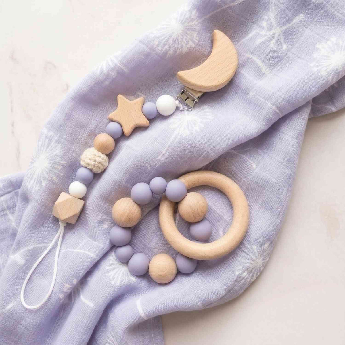 Particolare di catenella in silicone lilla e stelle in legno naturale, ideale come accessorio per neonata, su tessuto lilla morbido
