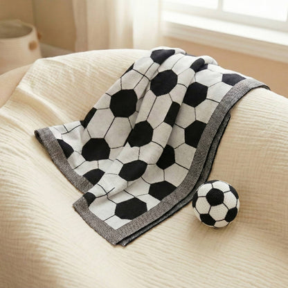 Coperta neonato a tema calcio in cotone, stesa su poltrona beige con pallone decorativo, ideale per neonati e appassionati di football.
