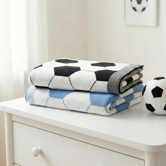 Coperta neonato a tema calcio in 100% cotone, piegata su cassettiera bianca, nei colori nero e azzurro, ideale per mezze stagioni.